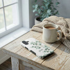 Handyhülle Glaube mit GELIEBT und Eucalyptus-Design auf iPhone neben Kaffeetasse und Strickdecke – Lifestyle